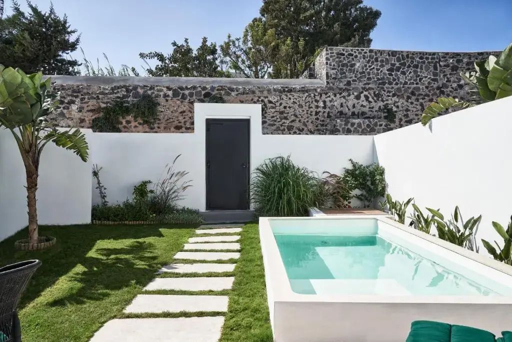 Privater Garten mit kleinem Pool und Steinmauer im Hintergrund.
