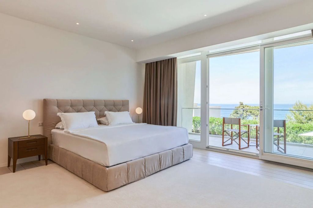 Helles Schlafzimmer mit modernem Doppelbett, Balkonzugang und atemberaubendem Meerblick.