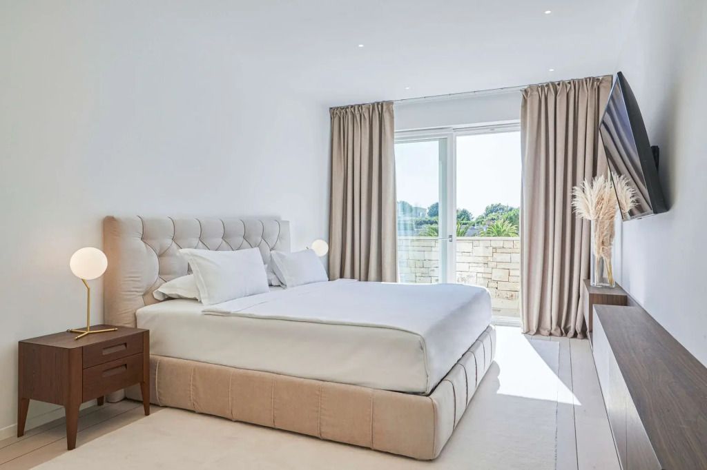 Schlafzimmer mit gepolstertem Bett, großen Fenstern und Zugang zur Terrasse mit Gartenblick.