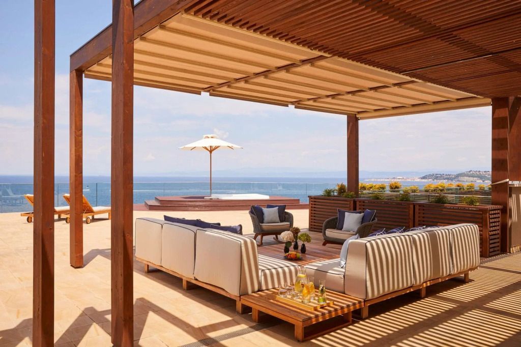 Terrasse mit Sitzgelegenheiten und Blick aufs Meer unter einem Sonnenschirm.