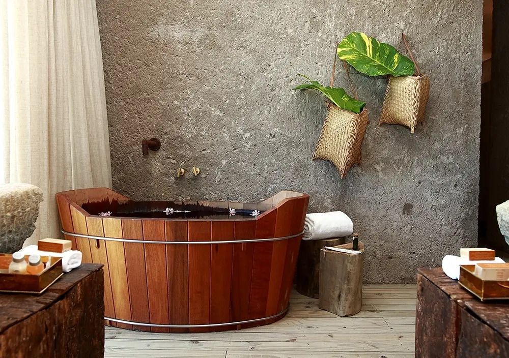 Holzbadewanne in stilvollem Design eingefügt in rustikaler Wand im Kenoa Resort