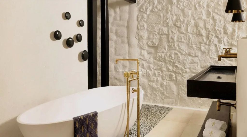 Moderne Badewanne mit goldenen Armaturen vor einer Steinwand