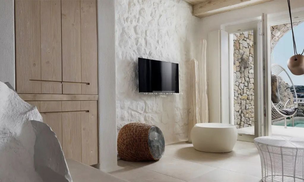 Lounge-Bereich der Suite mit TV und modernen Sitzgelegenheiten vor Steinwand.