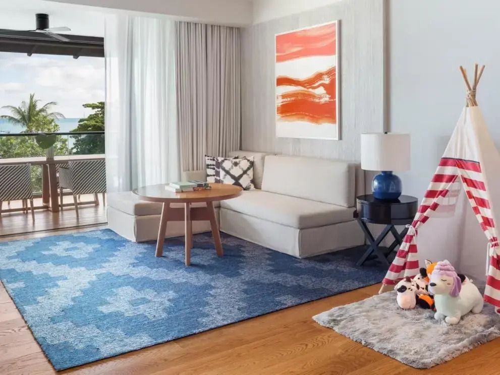 Heller Wohnbereich der Suite mit modernem Kunstwerk und Blick auf den Balkon.