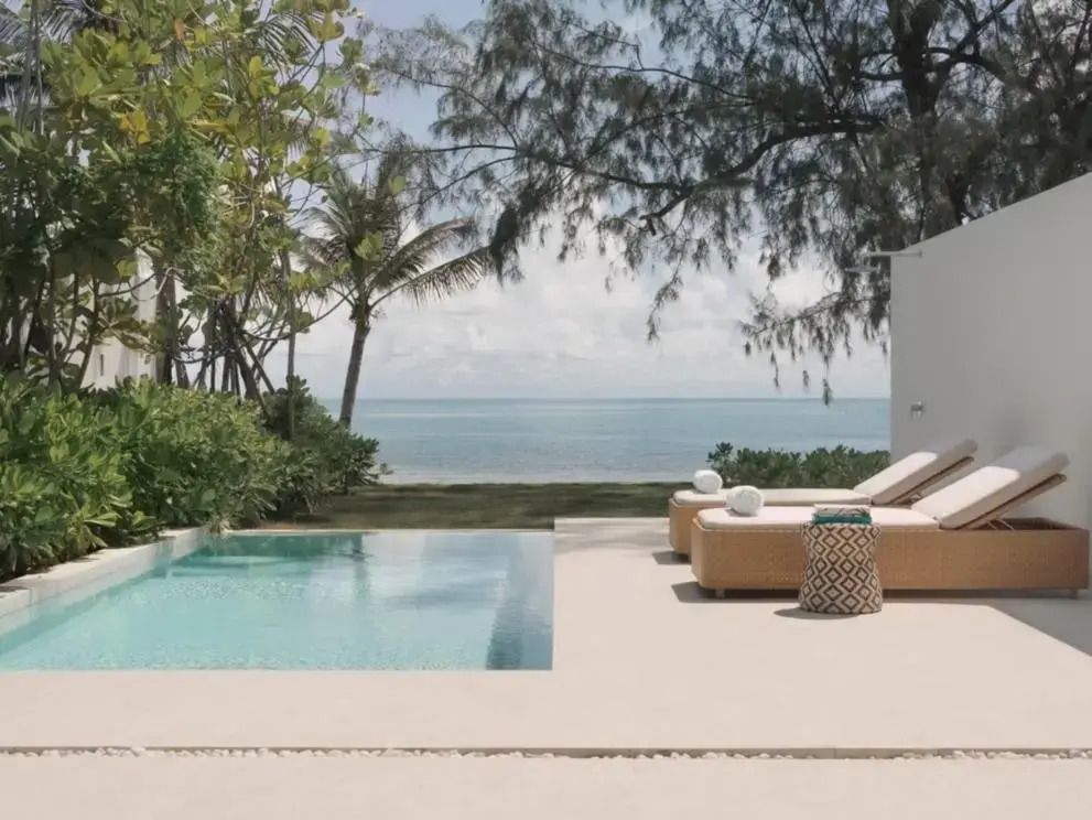 Privater Pool mit Sonnenliegen und Blick auf das Meer durch tropische Vegetation