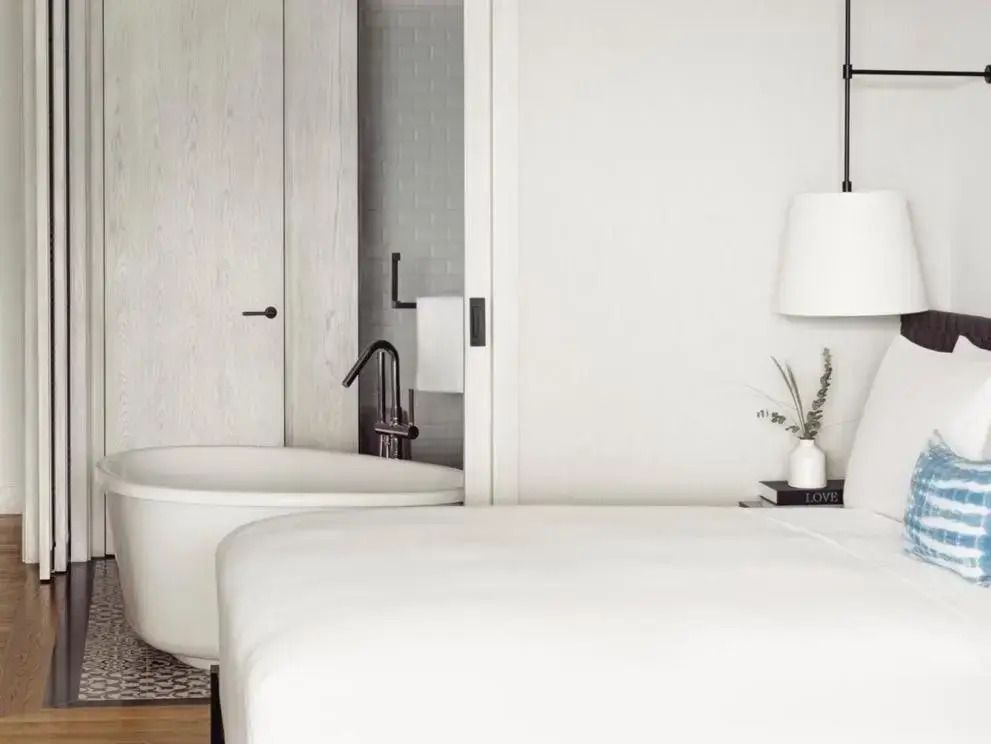 Doppelbett neben einer freistehenden Badewanne, minimalistisches Design