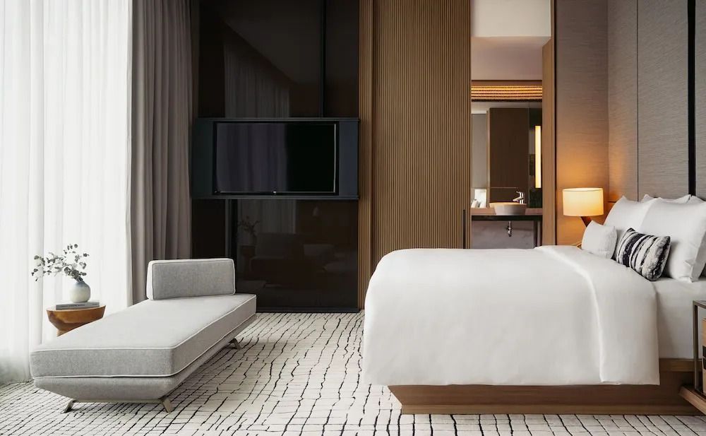 Modernes Schlafzimmer mit grauer Couch, eleganter Holzwand und großem Flachbildfernseher.