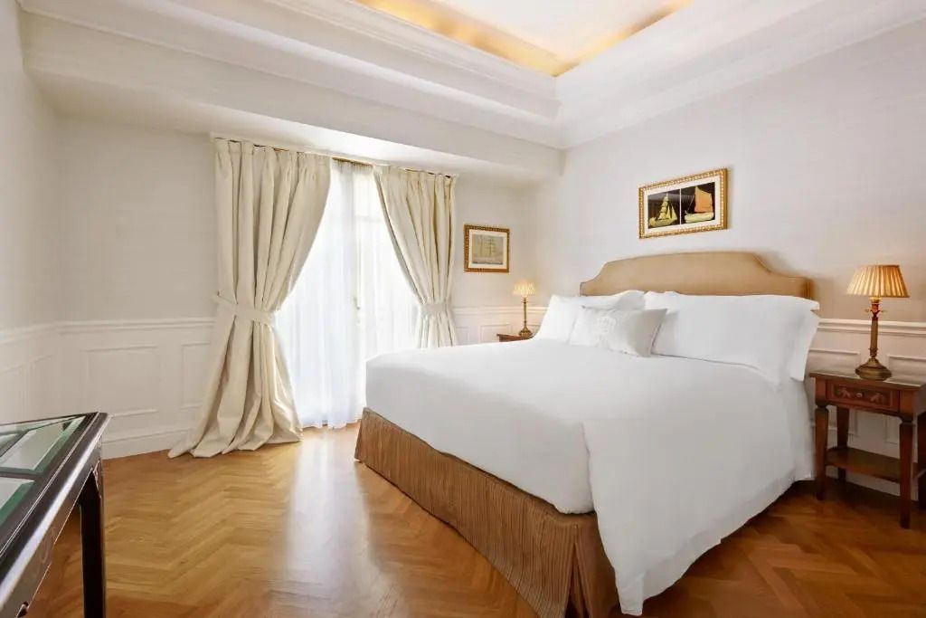 Helles Schlafzimmer mit Doppelbett, edlen Vorhängen und Holzboden in einem Hotel.