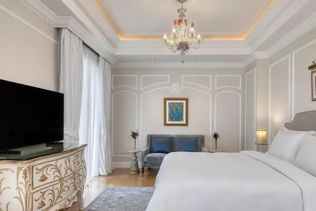 Helles Schlafzimmer mit Kronleuchter und reich verzierter Kommode