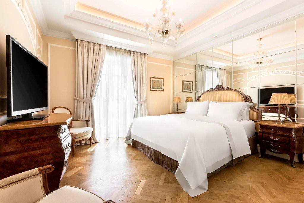 Elegantes Schlafzimmer mit großem Doppelbett und Deckenleuchter in heller Suite.