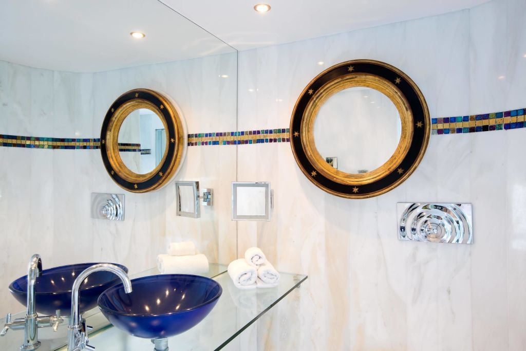 Elegantes Badezimmer mit blauem Waschbecken aus Glas und goldenen Spiegeln.