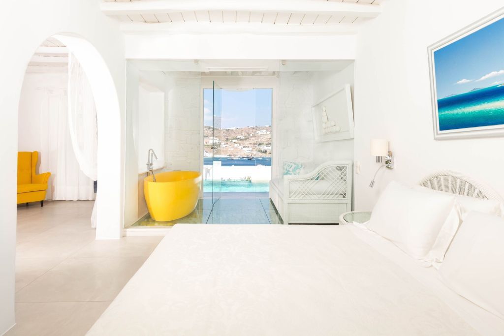 Helles Zimmer mit gelber Badewanne und Blick auf privates Pooldeck.