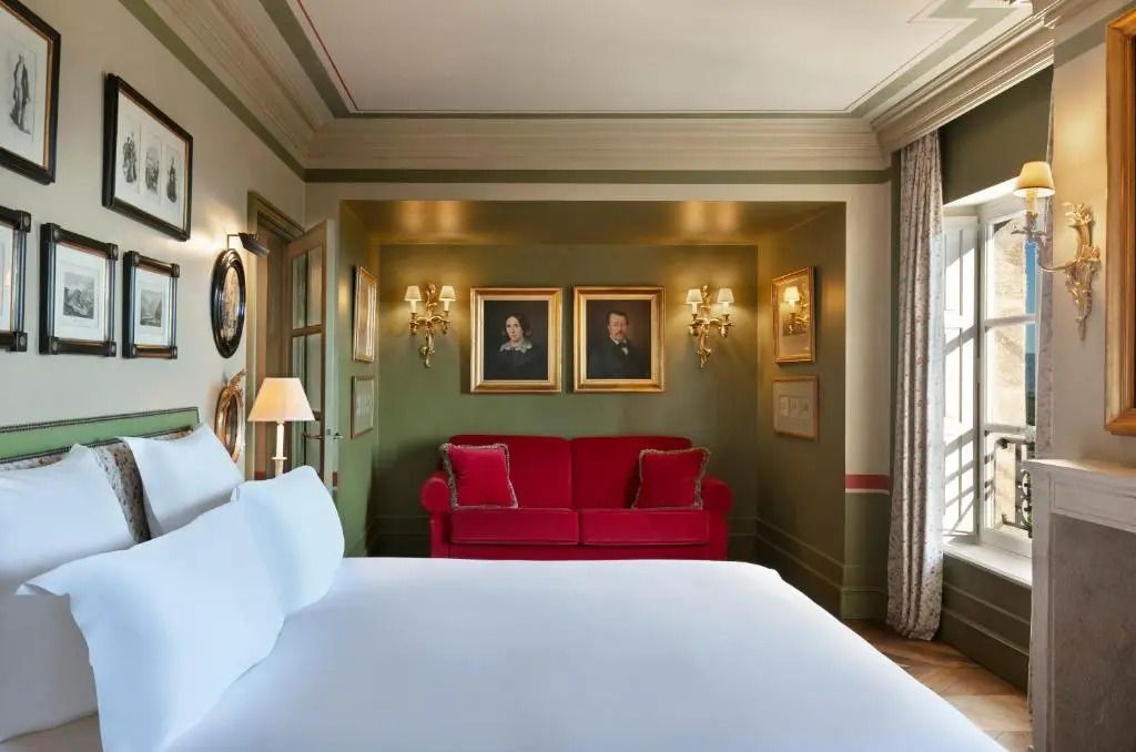 Zimmer mit weißem Bett und rotem Sofa, Kunstwerke an grüner Wand.