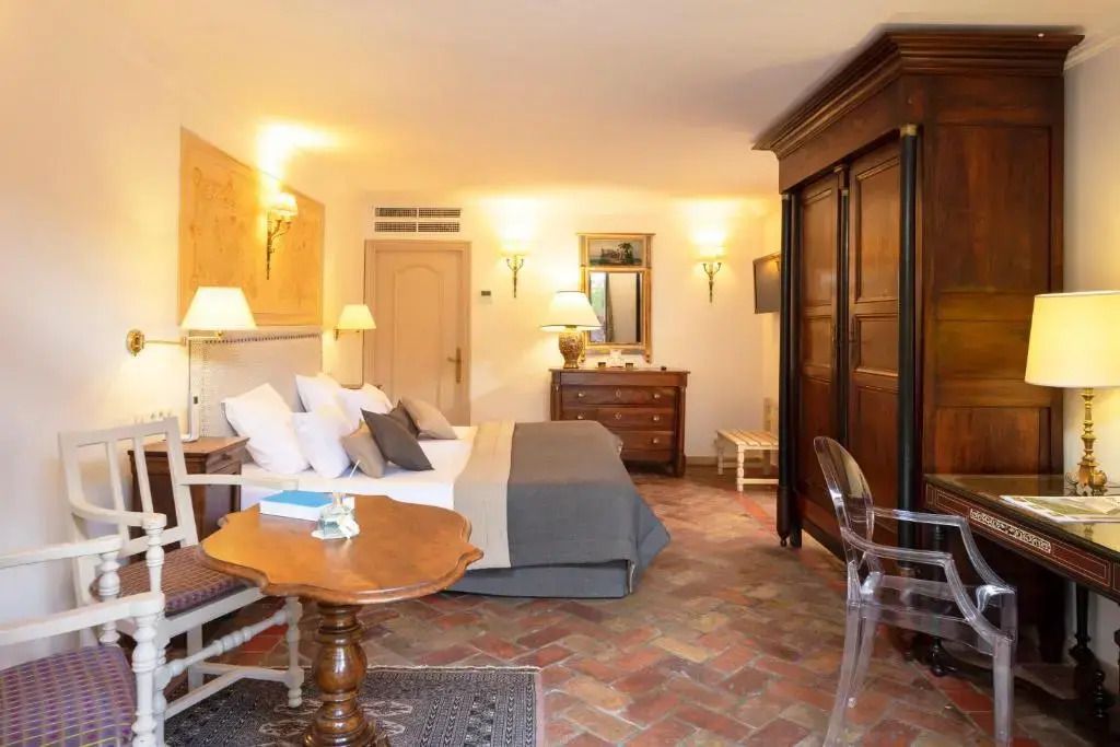 Helles Zimmer mit Bett und klassischem Holzmobiliar auf Fliesenboden