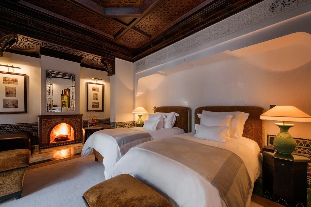 Riad-Schlafzimmer mit Doppelbetten und warmem Kamin in edler Atmosphäre