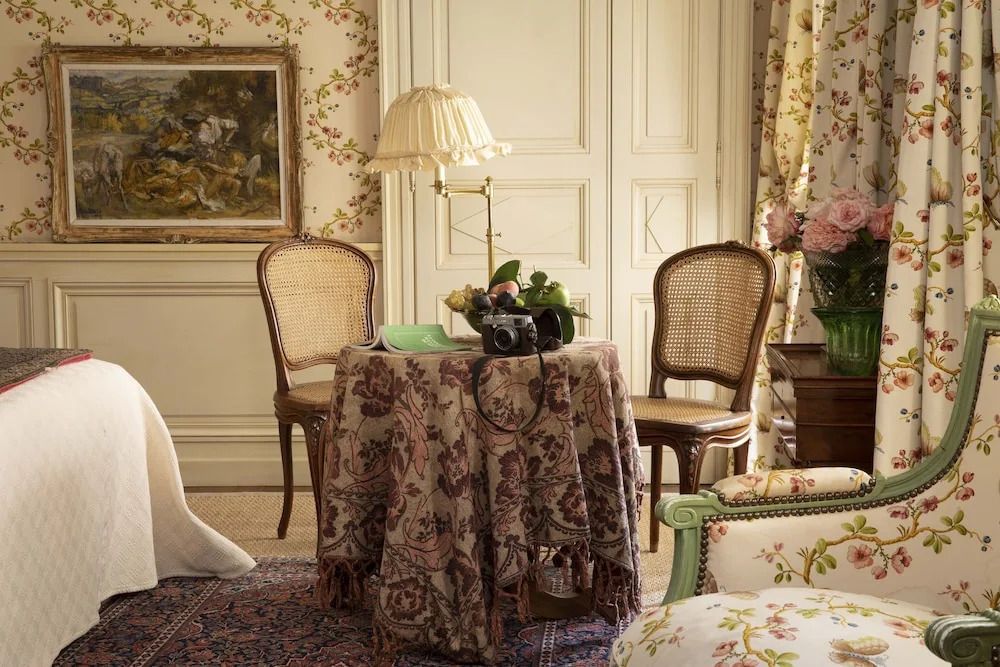 Sitzecke mit Tisch und stilvollen Stühlen, dekoriert mit Blumen und zarten Wandmustern.