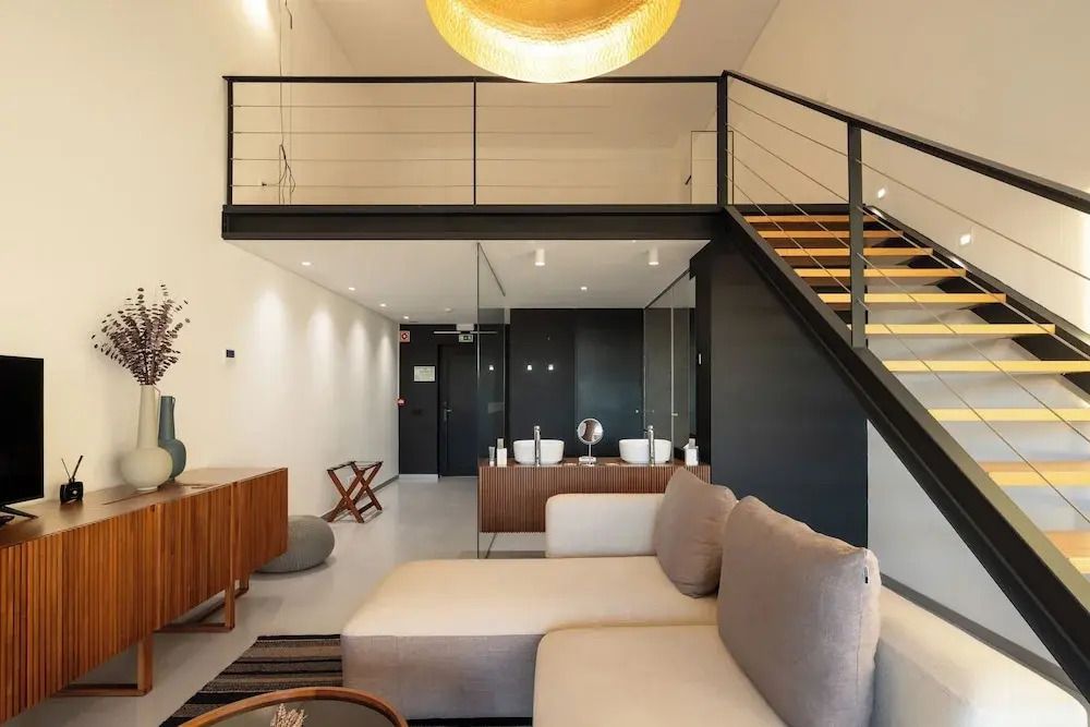 Modernes Zimmer mit offener Galerie. Sofa im Vordergrund, Holztreppe zur oberen Etage.