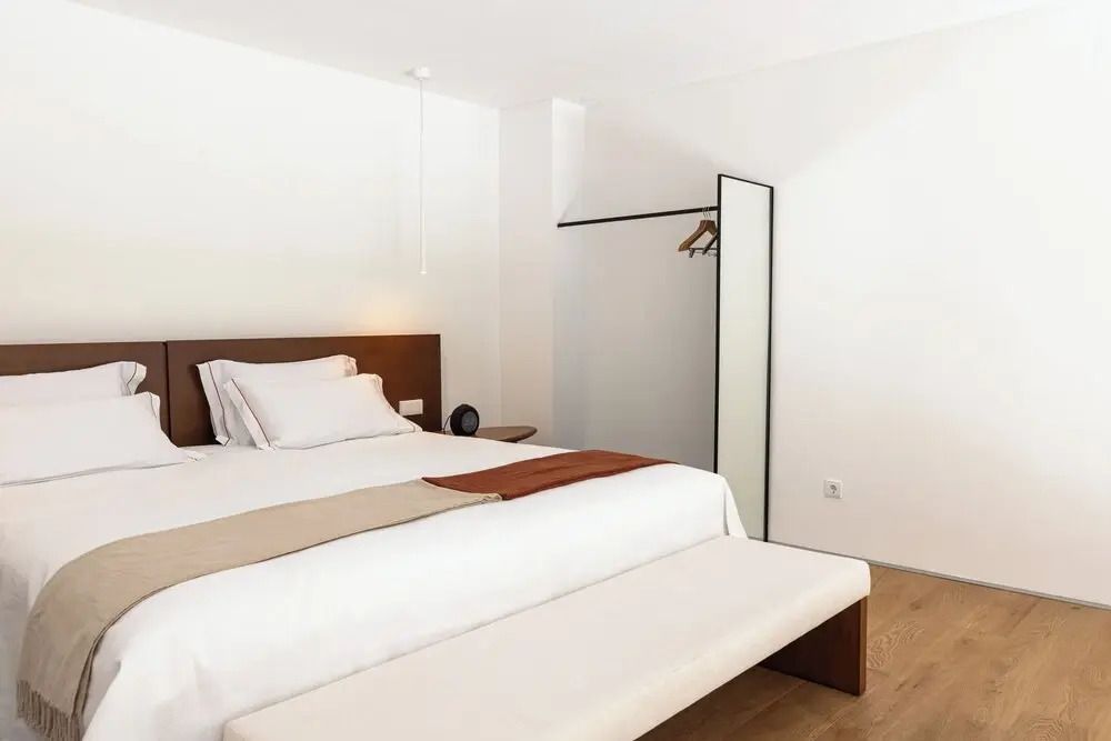 Helles Schlafzimmer mit Doppelbett in minimalistischen Design, Bank am Fußende.