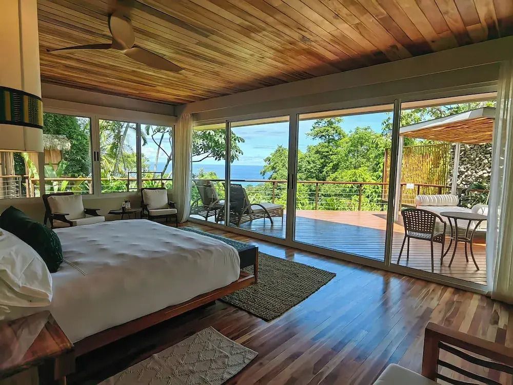 Geräumige Suite mit großem Bett und Aussicht auf den Ozean vom Balkon.