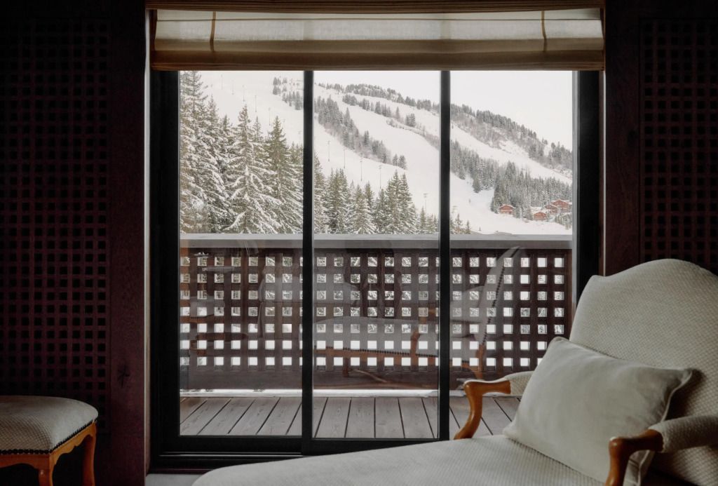 Fensterblick vom Bett aus auf den schneebedeckten Balkon und die umliegenden Berge.