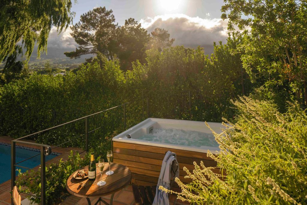 Privater Außenbereich der Fynbosch Hütte mit Jacuzzi und malerischem Ausblick bei Sonnenuntergang.