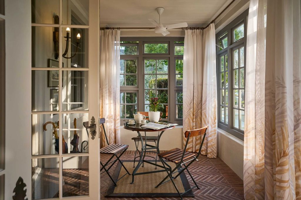 Heller Wintergarten mit Tisch, zwei Stühlen und großen Fenstern.