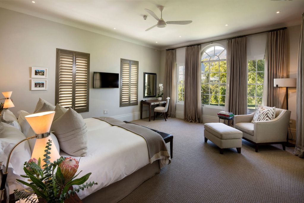 Zimmer im Leeu Estate mit großem Bett, Sessel und Fenster mit Gartenblick.