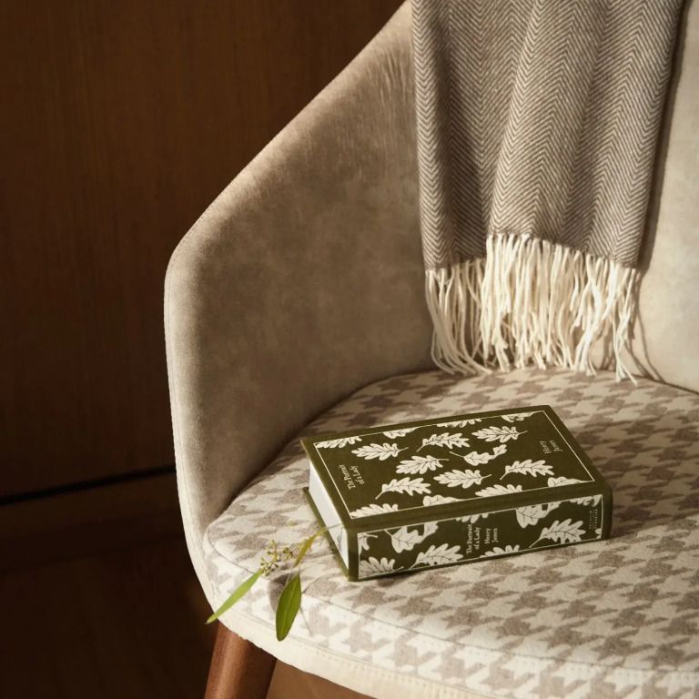 Eleganter Sessel mit einem Buch und einer Decke dekoriert in neutralen Tönen.