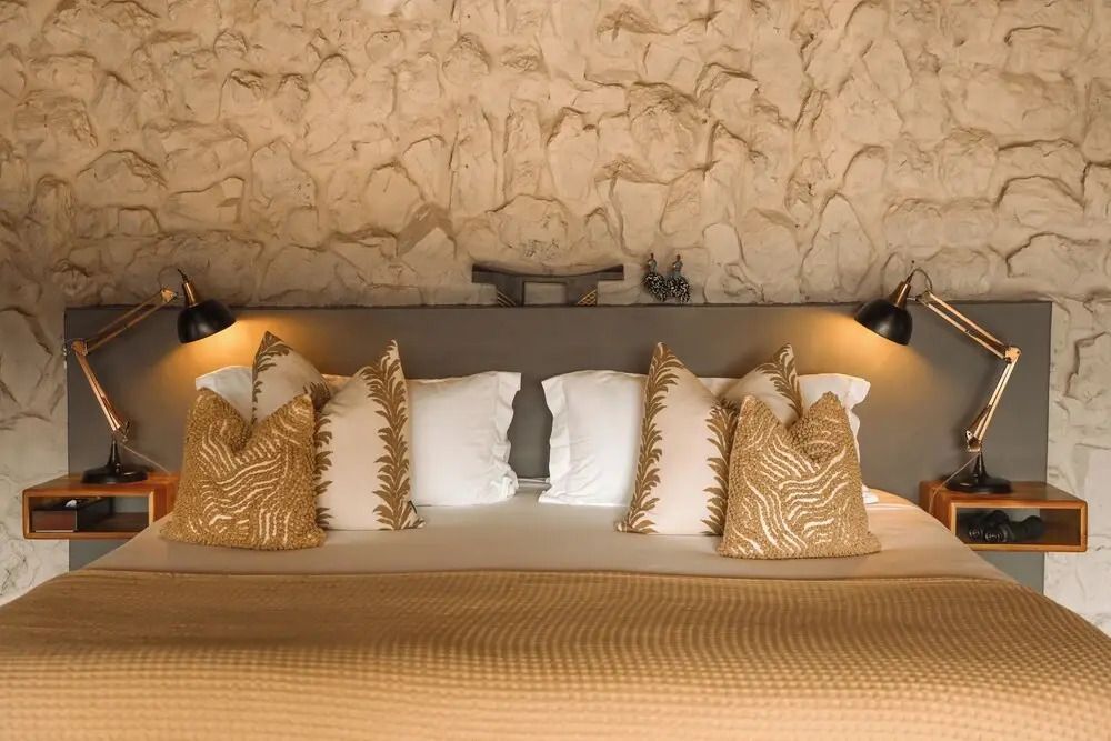 Komfortables Bett mit zahlreichen dekorativen Kissen und Steinwand