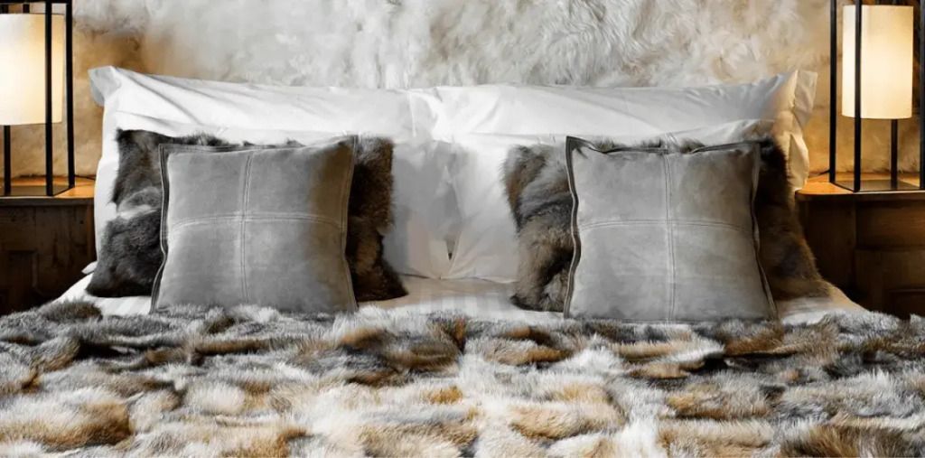 Bett mit flauschigen Decken und Kissen aus Kunstpelz in warmen Farbtönen.