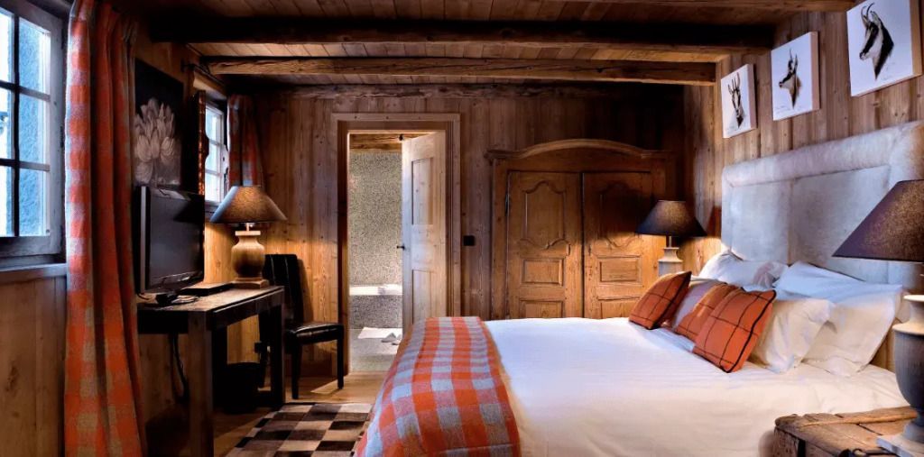 Rustikales Schlafzimmer mit Holzwänden, Doppelbett und Zugang zum Badezimmer.