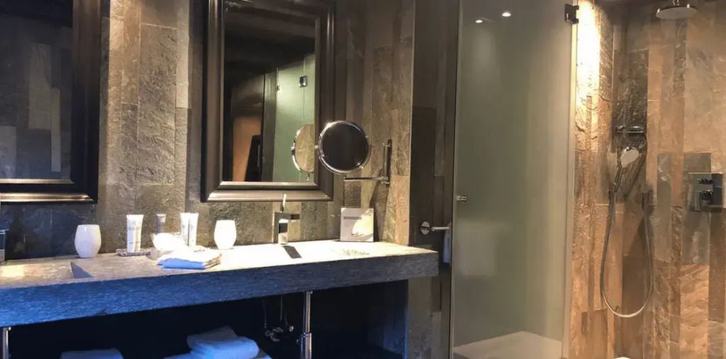 Modernes Badezimmer mit großem Spiegel, Waschtisch und Glasdusche in der Rochebrune Suite.