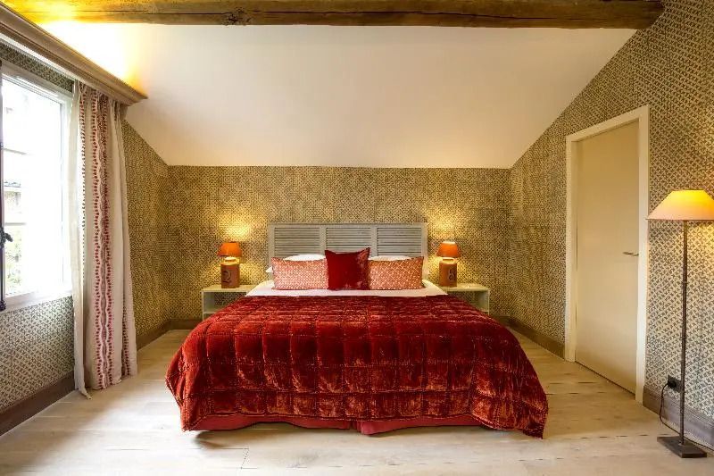 Großzügiges Schlafzimmer mit roter Bettdecke und Holzbalken