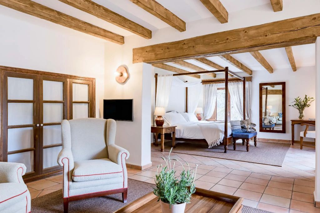 Junior-Suite mit Himmelbett und gemütlichem Sessel mit Holzbalkendecke