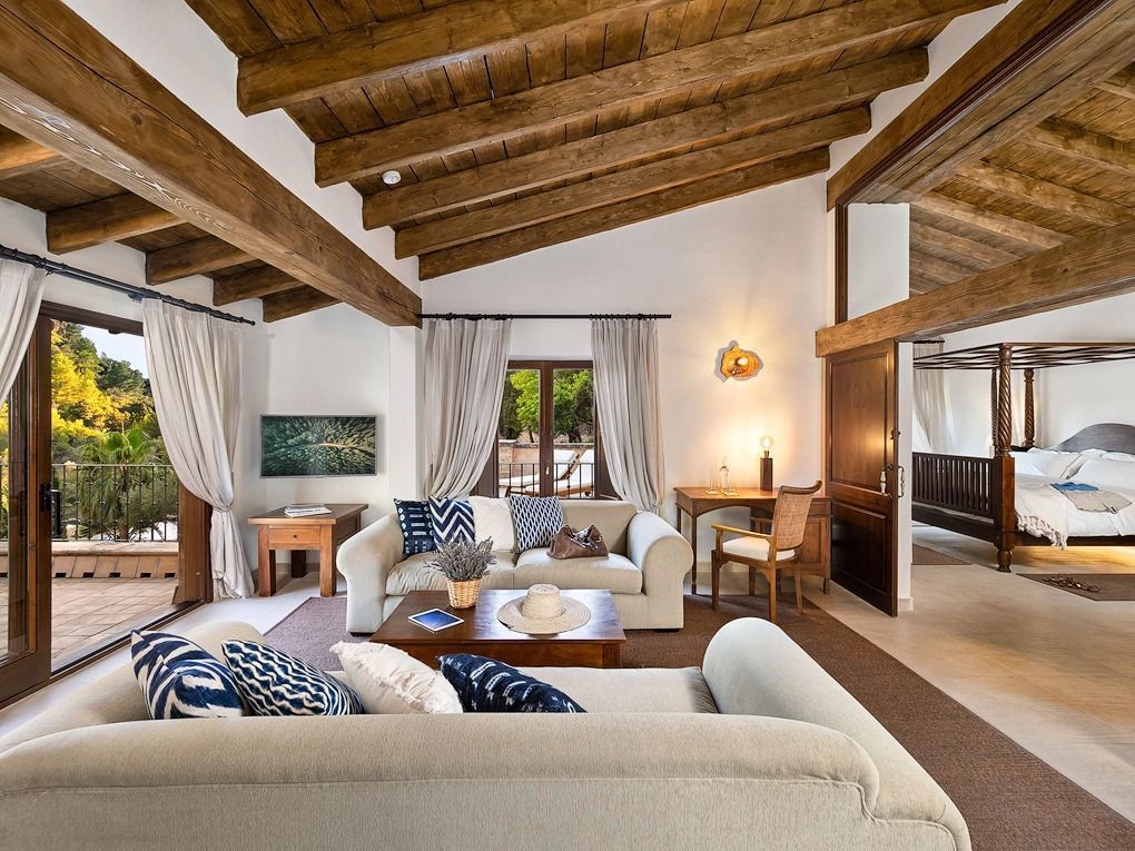 Luxuriöses Wohnzimmer mit Holzbalkendecke und gemütlichen Sofas vor großen Fenstern