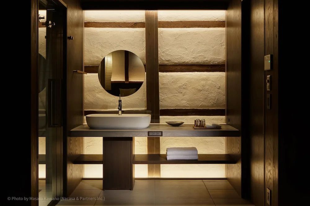 Modernes Badezimmer mit stilvoller Beleuchtung und rundem Spiegel im Loquat Nishi Izu.