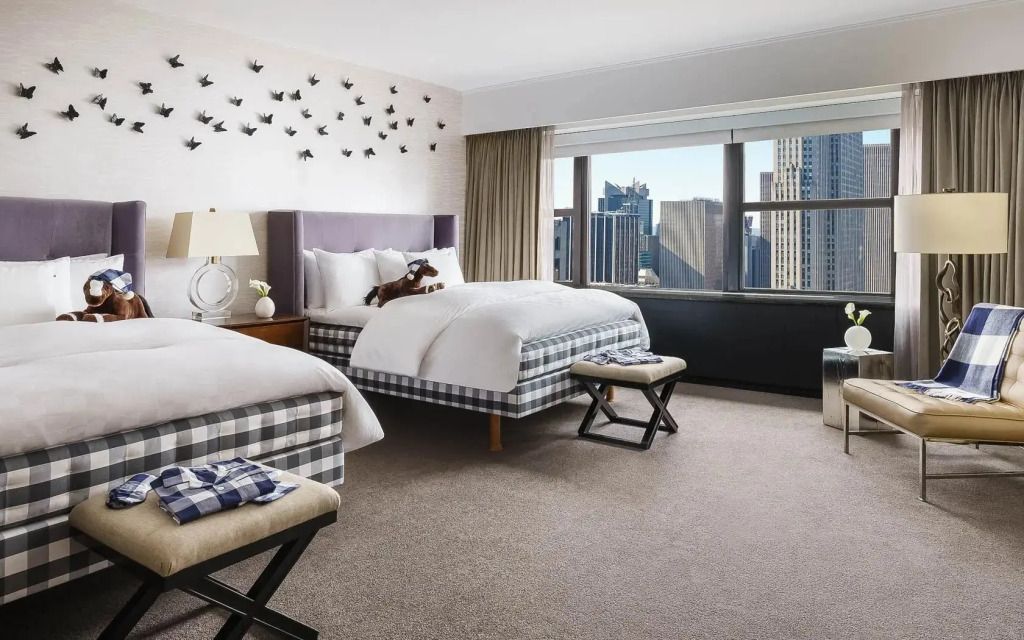 Suite mit zwei Betten und Blick auf die Skyline durch große Fenster.