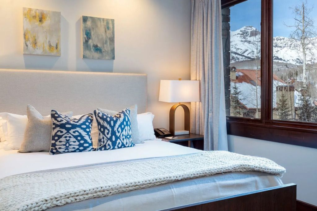 Gemütliches Schlafzimmer mit stilvollen Kissen und Fensterausblick auf schneebedeckte Berge.