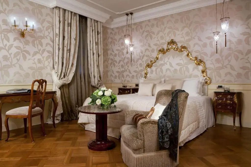 Elegantes Deluxe-Zimmer mit Doppelbett und floralen Tapeten, goldverziertem Kopfteil.