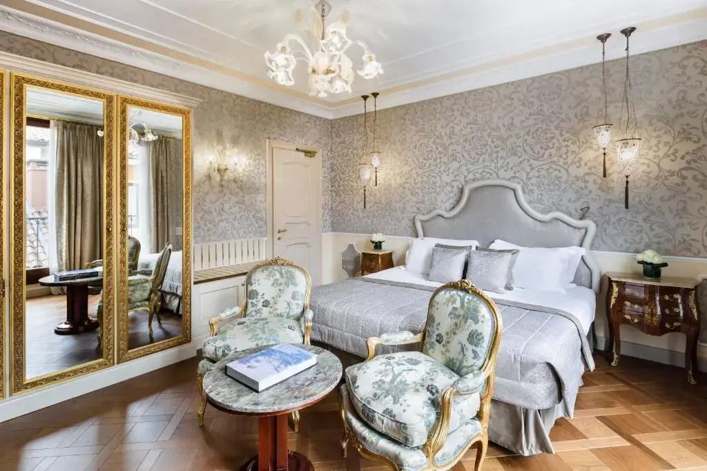 Helles Deluxe-Zimmer mit großem Spiegel, floralem Sesselpaar und antikem Tisch.