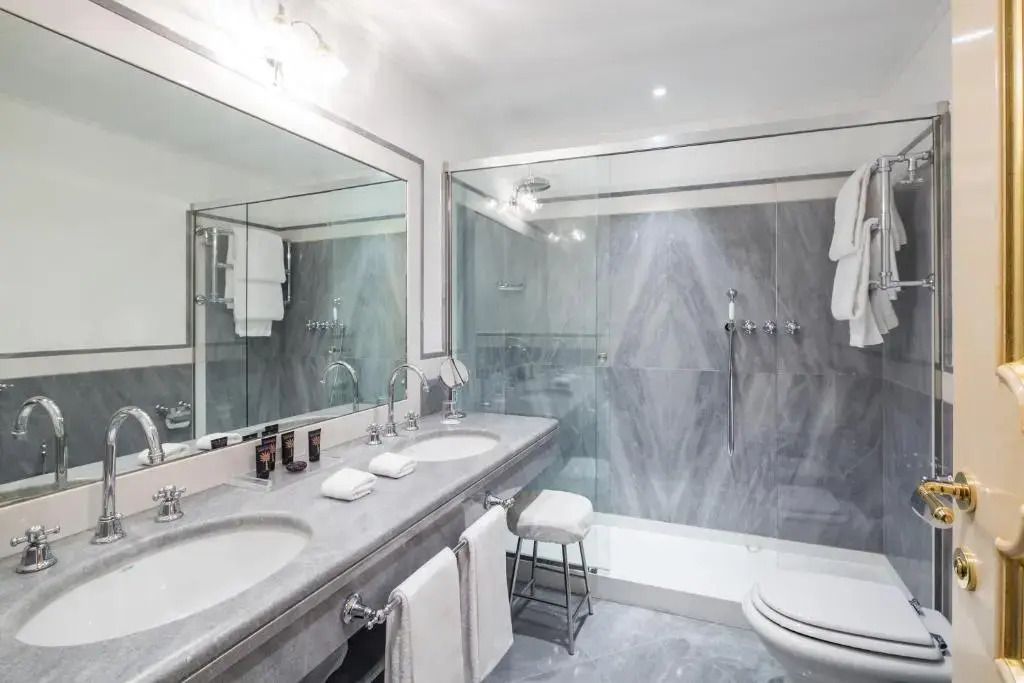 Modernes Badezimmer mit Doppelwaschbecken, großer Spiegelwand und Duschkabine aus Marmor.