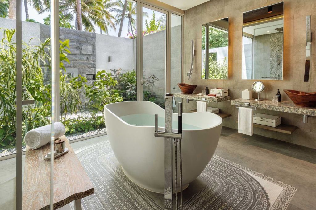 Modernes Badezimmer mit freistehender Badewanne und Blick auf einen tropischen Garten