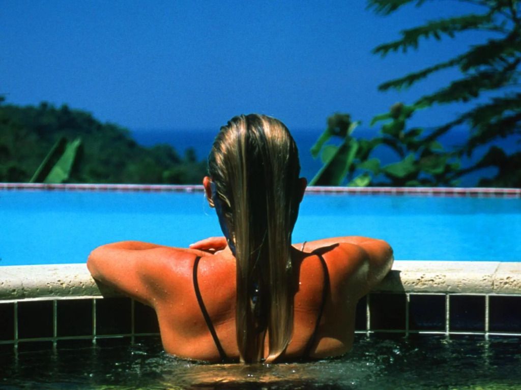 Frau genießt Infinity Pool mit Meerblick und tropischer Kulisse