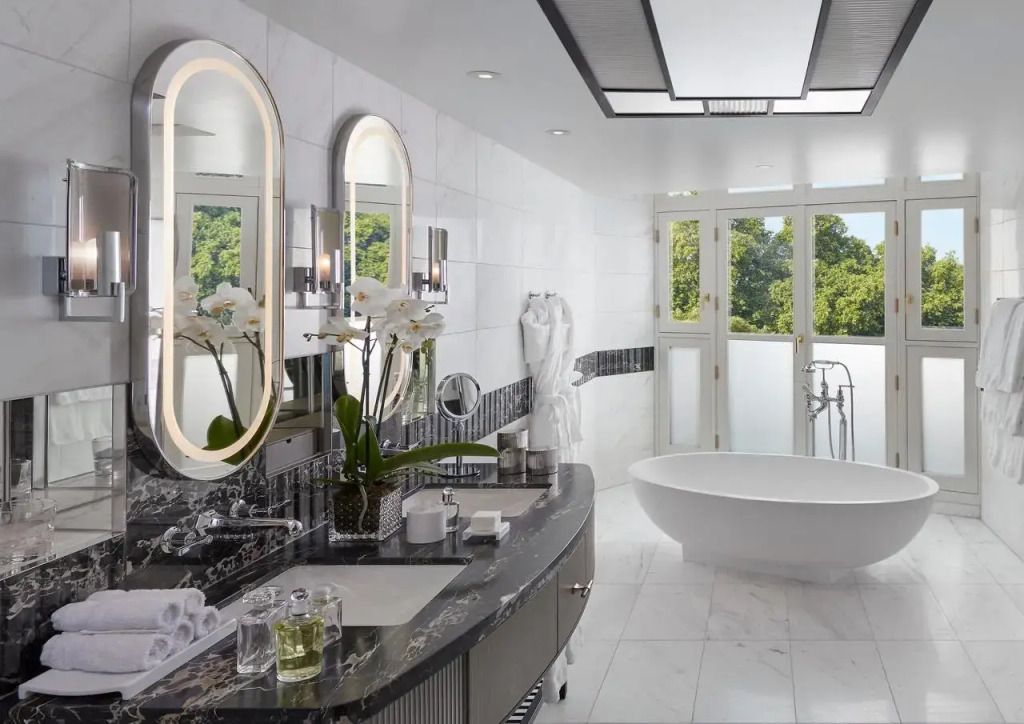 Großes, modernes Badezimmer mit freistehender Badewanne und Wandspiegeln, Parkblick durch Fenster