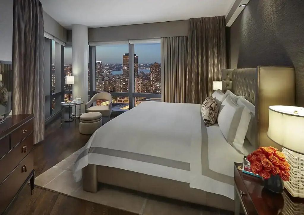 Modernes Schlafzimmer in hochgelegenem Suite mit Panorama-Nachtsicht auf New York.