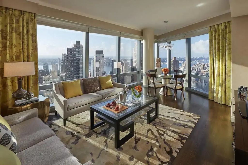 Wohnzimmer einer Suite mit Panoramafenstern und Blick auf New Yorks Skyline.