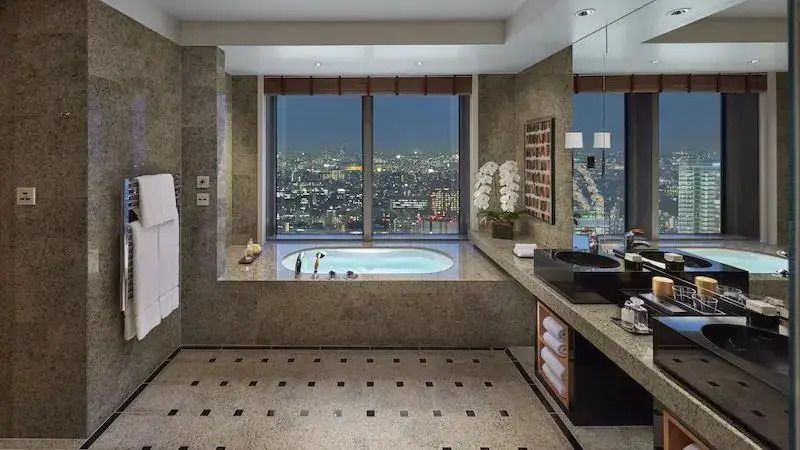 Badezimmer der Oriental Suite mit Whirlpool und nächtlichem Stadtpanorama