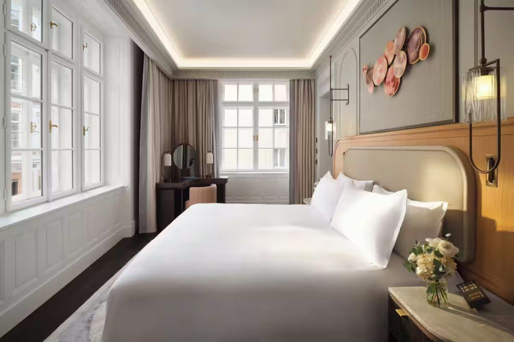 Helles Schlafzimmer mit großem Bett, Kunst an der Wand und Fenster mit Vorhängen.