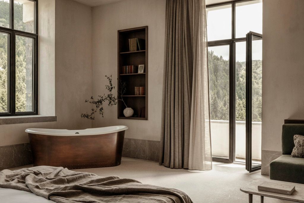 Helles Schlafzimmer mit freistehender Badewanne und Blick ins Grüne.