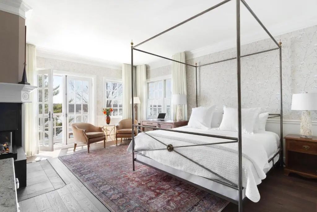 Hell eingerichtetes Zimmer mit Himmelbett, Sesseln und großem Fenster